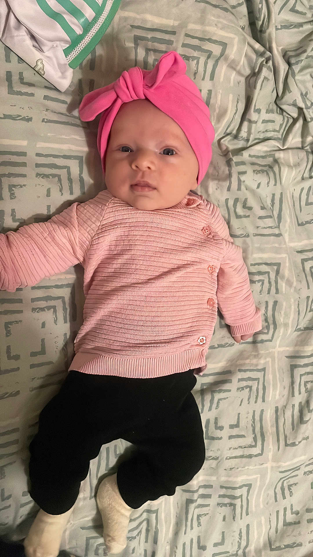 Jennah a rejoint le concours — aidez-le/la à gagner de superbes lots ! baby, infant, newborn, pink_hat, pink_sweater, black_pants, white_socks, bed, blanket, patterned_bedding, pillow, lying_down, portrait, face, eyes, cute, one_person, indoors, infant_clothing, baby_photo