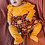 Heer is registered to the contest to win money with this photo: baby, infant, orange_clothing, headband, bow, halloween, pumpkin_pattern, blanket, lying_down, cute, child, person, toddler, festive, smiling, indoors, apparel, portrait, happy, fabric
