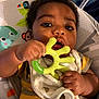 Messiah is registered to the contest to win money with this photo: baby, infant, teething_toy, bib, hand, face, curly_hair, bright_eyes, baby_seat, animal_print, elephant, monkey, colorful, clothing, striped_shirt, indoor, close_up, child, cute, portrait