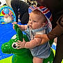 baby, child, infant, hat, colorful, inflatable_toy, green_toy, indoor, play_area, adult_hand, blue_mat, people, clothing, supporting_hand, face, cheeks, legs, eyes, toy, playtime