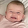 baby, smiling, infant, pink_clothing, happy, cute, face, lying_down, hand, skin, bed, pillow, blanket, child, person, young_child, indoors, portrait, closeup, joyful