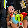 Carter is registered to the contest to win money with this photo: baby, car_seat, chicco, sunglasses, plush_toy, colorful_toy, striped_clothing, infant, child, seatbelt, foot, hand, face, blue_eyes, brick_wall, warning_label, indoor, cute, comfort, photography