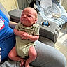 newborn, baby, infant, person, adult, clothing, onesie, sitting, indoor, furniture, baby_rocker, toy, chair, legs, hand, face, expression, light, cozy, home