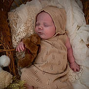 Oliver is registered to the contest to win money with this photo: baby, sleeping, knit_outfit, bonnet, teddy_bear, wicker_basket, blanket, soft_fabric, cozy, infant, cute, peaceful, portrait, child, resting, hand, foot, texture, warm_colors, indoor