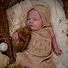 baby, sleeping, knit_outfit, bonnet, teddy_bear, wicker_basket, blanket, soft_fabric, cozy, infant, cute, peaceful, portrait, child, resting, hand, foot, texture, warm_colors, indoor