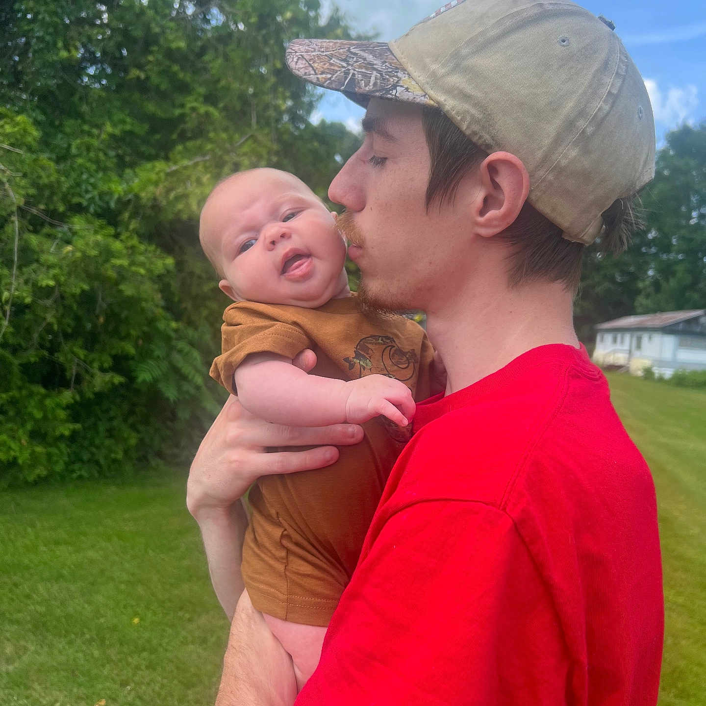 Paisleigh is registered to the contest to win money with this photo: affection, baby, brown_clothing, cap, child, clouds, daylight, family, grass, greenery, holding, kiss, love, man, nature, outdoor, portrait, red_shirt, sky, trees