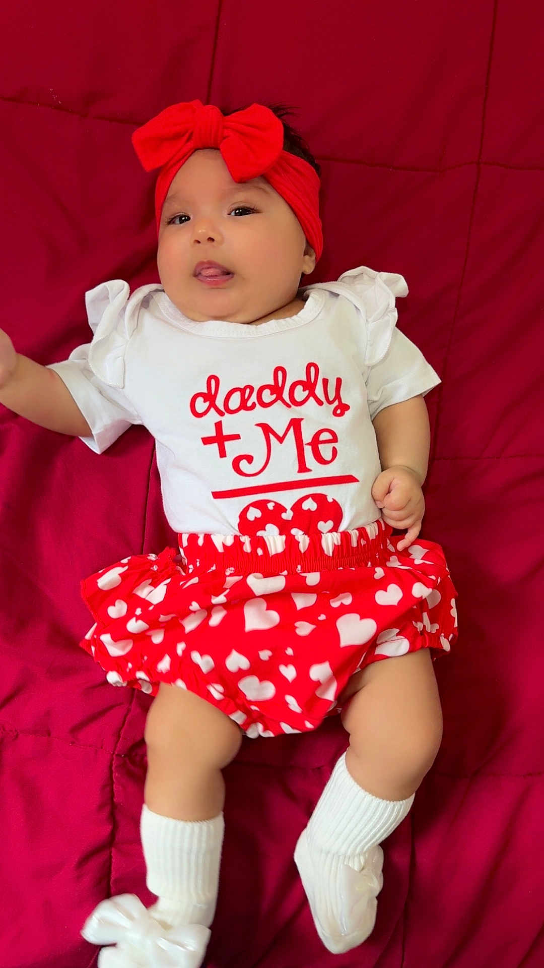 Valentina is registered to the contest to win money with this photo: baby, infant, red_headband, white_shirt, heart_pattern, red_skirt, white_socks, bow, cute, lying_down, tongue_out, child, portrait, indoor, soft_fabric, smiling, person, closeup, adorable, playful