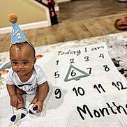 Kylen is registered to the contest to win money with this photo: baby, infant, six_months, milestone_blanket, party_hat, sitting, onesie, socks, indoor, hardwood_floor, portrait, smile, numbers, triangle_marker, celebration, staircase, decorations, photography, playtime, cute