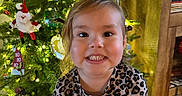Veronica joined the competition — help win amazing prizes! child, smiling, leopard_print, shirt, christmas_tree, ornaments, lights, holiday, indoor, decorations, festive, tree, face, person, happy, young_child, home, photography, wooden_floor, furniture