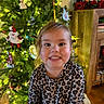 child, smiling, leopard_print, shirt, christmas_tree, ornaments, lights, holiday, indoor, decorations, festive, tree, face, person, happy, young_child, home, photography, wooden_floor, furniture