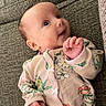 baby, infant, smiling, face, hand, clothing, onesie, floral_pattern, couch, textured, fabric, person, child, cute, portrait, indoor, young, skin, head, expression