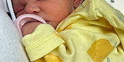 Raylynn is registered to the contest to win money with this photo: baby, newborn, sleeping, yellow_clothing, onesie, infant, person, hand, car_interior, window, closeup, peaceful, cute, resting, skin, head, ear, soft, tender, caring