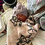 newborn, baby, blanket, hat, bow, sleeping, hospital_gown, adult, bed, fan, indoor, resting, comfort, patterned, soft, cozy, person, infant, closeup, cute