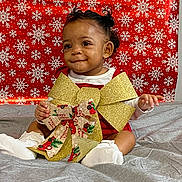 Z'Yane joined the competition — help win amazing prizes! baby, child, smile, curly_hair, socks, red_outfit, gold_bow, christmas_ribbon, holiday, snowflake_pattern, red_background, gray_blanket, festive, indoors, portrait, cute, sitting, happy, celebration, person
