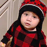 Paxton is registered to the contest to win money with this photo: black, cabinet, checkered_pattern, child, clothing, curious, expression, face, floor, hand, hat, indoor, knit_hat, person, portrait, red, sweater, toddler, warm_clothing, young_child