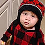 black, cabinet, checkered_pattern, child, clothing, curious, expression, face, floor, hand, hat, indoor, knit_hat, person, portrait, red, sweater, toddler, warm_clothing, young_child