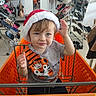 Alex is registered to the contest to win money with this photo: toddler, child, shopping_cart, santa_hat, tiger_shirt, blue_eyes, shopping_store, shoes, handbags, clothing, orange_cart, retail, rack, footwear, person, cute, indoor, smile, baby, holiday