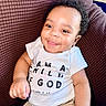 Asaiah joined the competition — help win amazing prizes! baby, child, smiling, curly_hair, white_shirt, text_on_shirt, cushion, brown_cushion, seated, happy, indoors, closeup, portrait, person, infant, cute, skin, hand, comfortable, cozy
