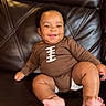 baby, brown_onesie, child, couch, cute, face, foot, hand, happy, indoors, infant, leather_couch, one_person, plush, portrait, relaxed, seated, skin, smiling, young_child