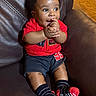 baby, black_shorts, bright_colors, child, clapping, couch, cute, hair, happy, indoor, infant, leather_couch, person, portrait, red_shirt, seated, skin, smiling, socks, striped_socks