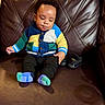 Asaiah is registered to the contest to win money with this photo: baby, child, sitting, colorful_sweater, knitted, socks, shoes, leather_couch, brown_couch, indoor, cute, portrait, young_child, clothing, footwear, person, cozy, comfortable, baby_fashion, casual