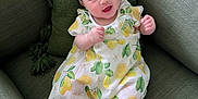 Eliana is registered to the contest to win money with this photo: baby, infant, smiling, lemon_print, dress, headband, bow, couch, green_pillow, tassel, legs, toes, sitting, indoor, portrait, cute, happy, fabric, pattern, person