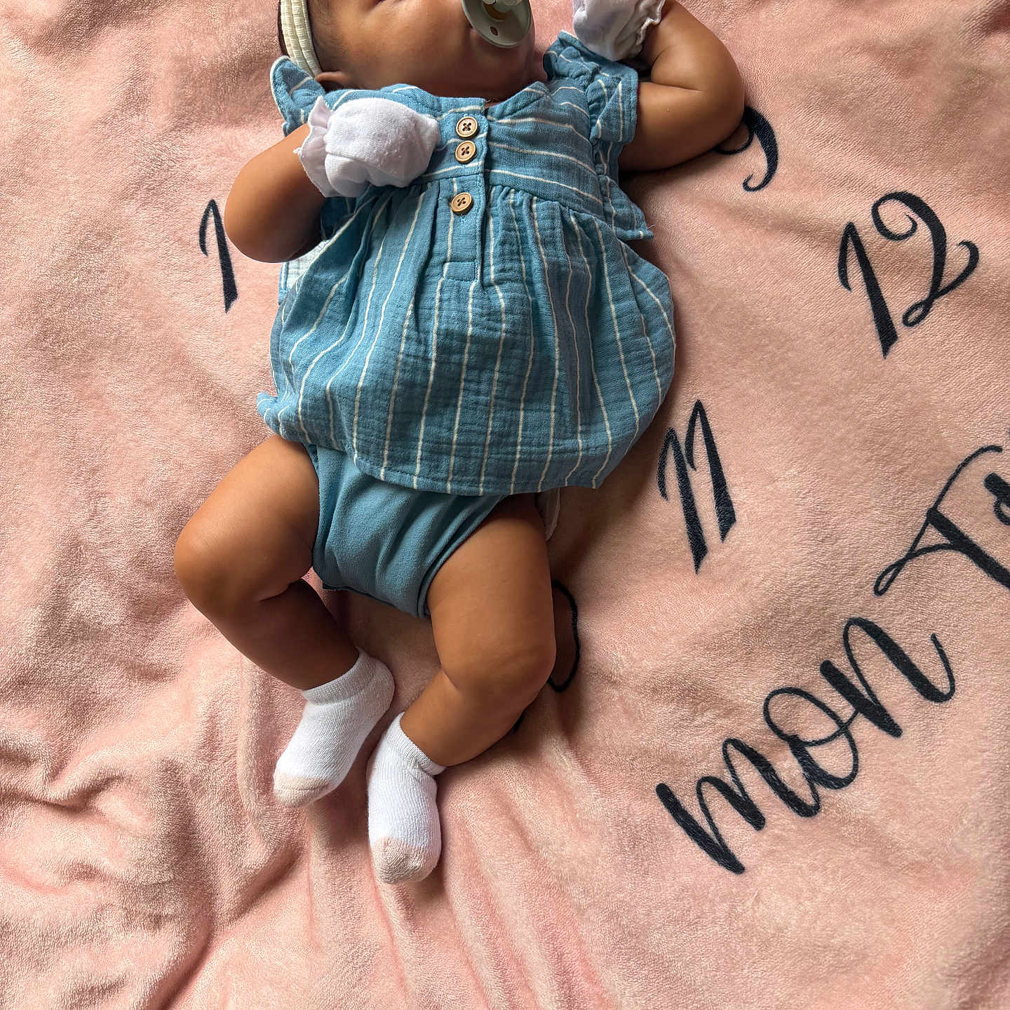 Kymora is registered to the contest to win money with this photo: adorable, baby, blanket, blue_dress, child, comfortable, cute, headband, indoor, infant, lying_down, mittens, newborn, numbers, pacifier, pink_blanket, portrait, soft_texture, text, white_socks