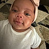 Kymora is registered to the contest to win money with this photo: baby, child, closeup, couch, cute, expression, eyes, fabric, face, headband, indoor, infant, patterned_couch, person, pink, portrait, skin, smile, soft_lighting, white_onesie