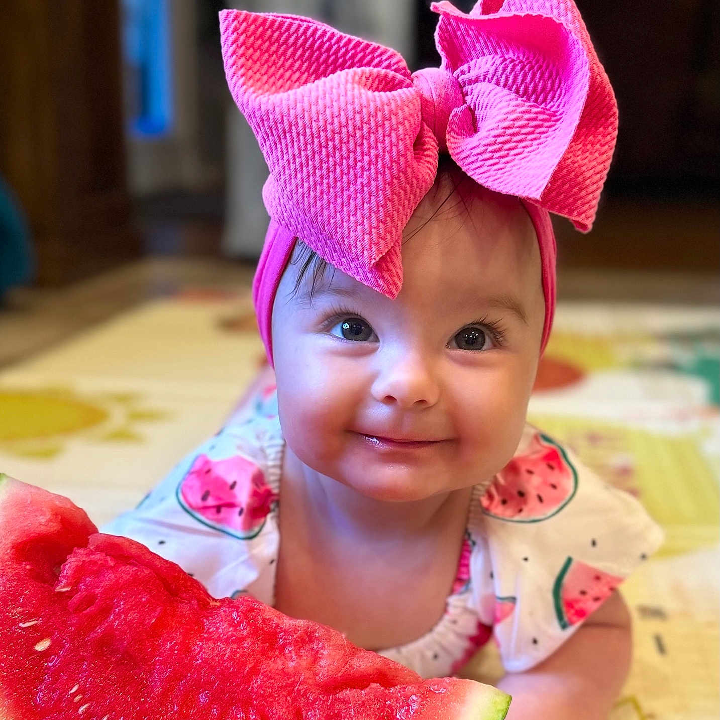 Emma is registered to the contest to win money with this photo: baby, child, closeup, colorful_mat, crawling, cute, cute_outfit, face, food, fruit, happy, headband, indoor, infant, person, pink_bow, playful, smiling, summer, watermelon