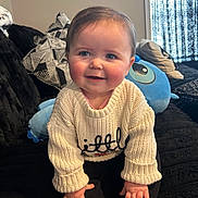 Sophia joined the competition — help win amazing prizes! baby, black, blue, child, couch, cozy, curtain, cute, face, hands, head, indoor, knitwear, person, pillow, plush_toy, seated, smiling, sweater, window