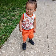 Marquis is registered to the contest to win money with this photo: toddler, child, sidewalk, grass, orange_shorts, tank_top, t_rex, curly_hair, black_shoes, outdoor, street, urban, casual_clothing, summer, young_child, portrait, walking, cute, daytime, person