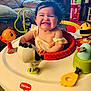 Scarlett is registered to the contest to win money with this photo: activity_center, baby, child, clothing, colorful, cute, face, fun, furniture, happy, indoor, infant, joy, living_room, plastic, play, seat, smiling, television, toy