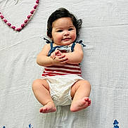 Scarlett is registered to the contest to win money with this photo: baby, infant, smiling, lying_down, diaper, striped_clothing, black_hair, hand_clasp, pink_beads, heart_shape, white_blanket, cute, chubby_cheeks, portrait, child, happy, soft_lighting, indoors, close_up, person