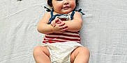 Scarlett is registered to the contest to win money with this photo: baby, black_hair, child, chubby_cheeks, close_up, cute, diaper, hand_clasp, happy, heart_shape, indoors, infant, lying_down, person, pink_beads, portrait, smiling, soft_lighting, striped_clothing, white_blanket