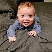 Trace is registered to the contest to win money with this photo: baby, smiling, blue_clothing, bed, blanket, infant, cute, happy, child, toddler, indoors, portrait, face, skin, sleepwear, hands, expression, lying_down, young_child, cozy