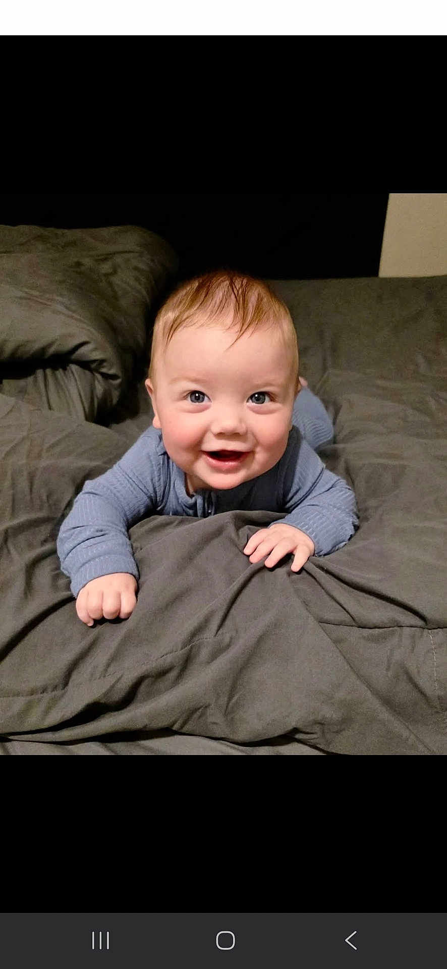 Trace is registered to the contest to win money with this photo: baby, smiling, blue_clothing, bed, blanket, infant, cute, happy, child, toddler, indoors, portrait, face, skin, sleepwear, hands, expression, lying_down, young_child, cozy