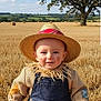 baby, blue_sky, child, face_paint, farm, grass, hay_bales, nature, outdoor, overalls, patches, portrait, rural, scarecrow_costume, smiling, straw, straw_hat, sunny, tree, wheat_field