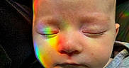 Willow is registered to the contest to win money with this photo: baby, infant, sleeping, closed_eyes, face, portrait, rainbow, colored_light, reflection, cozy, clothing, gray_shirt, closeup, indoors, soft_lighting, serene, peaceful, young_child, head, photography