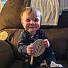 baby, child, couch, blanket, wooden_sign, onesie, socks, smile, indoor, furniture, face, person, happy, seated, home, cozy, infant, holding, toy, window