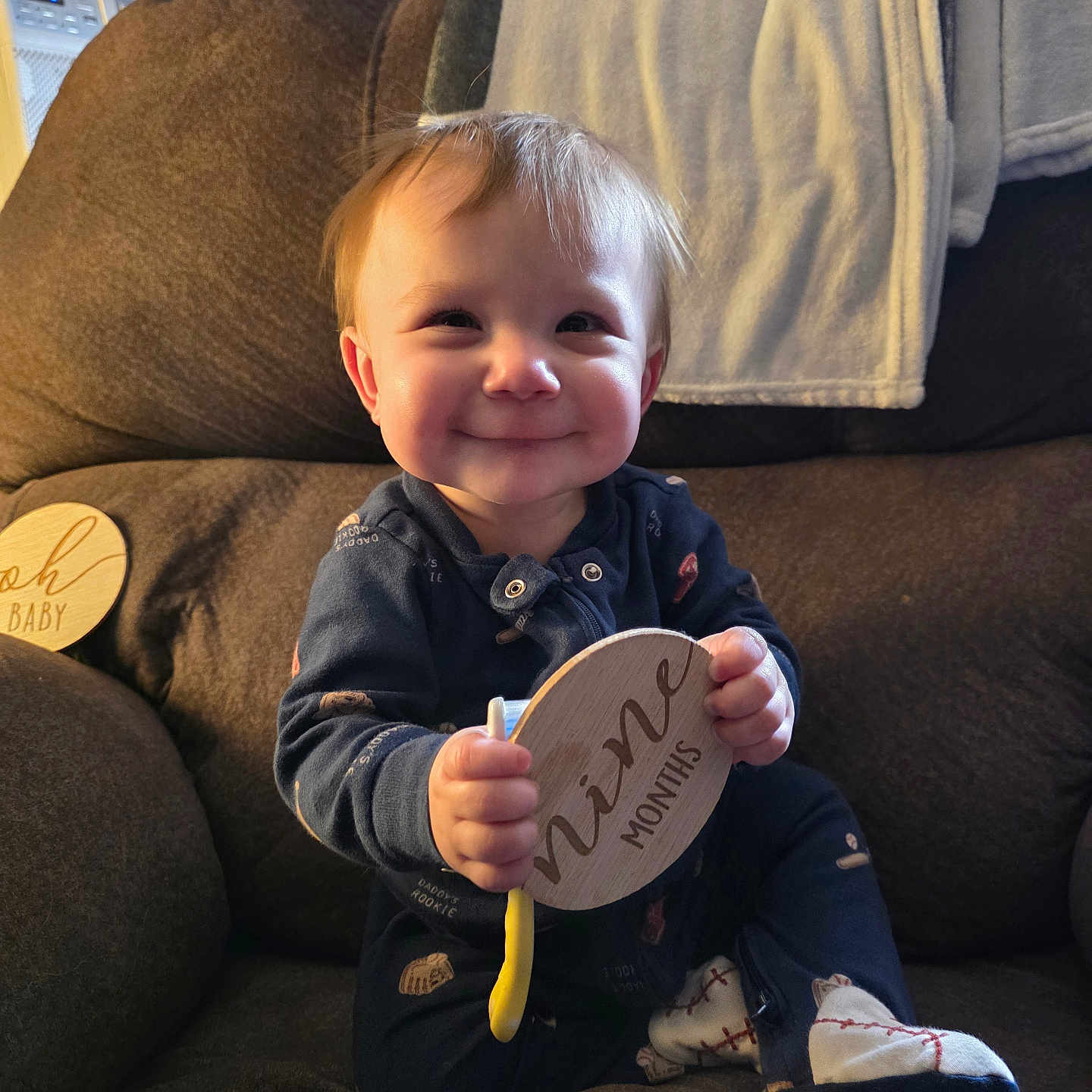 George joined the competition — help win amazing prizes! baby, child, couch, blanket, wooden_sign, onesie, socks, smile, indoor, furniture, face, person, happy, seated, home, cozy, infant, holding, toy, window