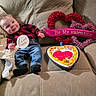 baby, infant, couch, valentines_day, heart_shaped_cake, wreath, plaid_shirt, jeans, sock, smiling, face, celebration, holiday, decoration, candle, love, cute, indoor, cozy, person
