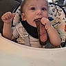George is registered to the contest to win money with this photo: baby, child, high_chair, steak, food, eating, indoor, cute, person, face, hand, clothing, bib, pattern, cushion, furniture, table, meal, dining, curious