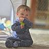 toddler, child, baby, onesie, blue_clothing, toy, carpet, indoor, smiling, happy, sitting, cute, face, young_child, playful, cozy, soft_light, blurred_background, home, person