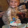 George joined the competition — help win amazing prizes! baby, child, smile, face, cake, birthday_candle, pajamas, dinosaur_pattern, plate, hand, indoor, celebration, happy, sitting, toy, blanket, furniture, person, food, cute