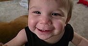 George is registered to the contest to win money with this photo: toddler, child, smile, happy, face, indoor, living_room, toy, furniture, carpet, person, clothing, short_sleeve, hair, cute, baby, expression, close_up, portrait, black_shirt
