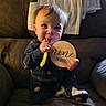George joined the competition — help win amazing prizes! baby, child, infant, armchair, blanket, wooden_sign, spoon, smiling, indoors, cozy, clothing, person, cute, young_child, face, sitting, home, soft_lighting, happy, portrait