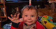 George joined the competition — help win amazing prizes! baby, child, smiling, waving, activity_center, toys, indoor, television, screen, furniture, living_room, person, happy, cute, infant, colorful, play, expression, clothing, hand