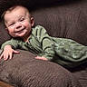 baby, smile, green_onesie, couch, brown_cushion, infant, relaxing, happy, child, indoor, portrait, hand, face, cozy, young_child, cute, home, resting, furniture, expression
