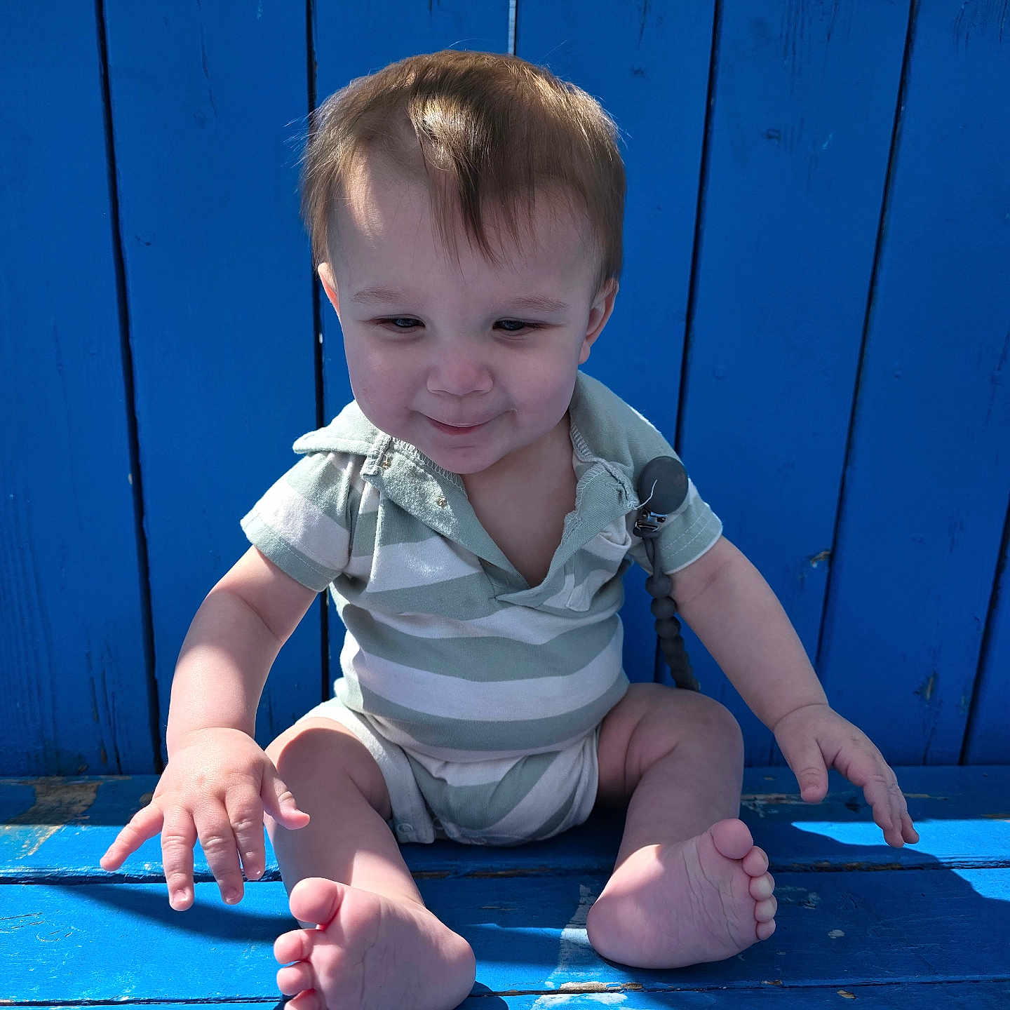 George joined the competition — help win amazing prizes! baby, child, infant, blue_bench, wood, outdoor, sunlight, striped_clothing, onesie, feet, toes, smile, face, hair, nature, tree, greenery, playful, sitting, person