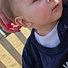 George is registered to the contest to win money with this photo: baby, child, face, portrait, person, hand, sandy_beach, clothing, shirt, foot, outdoor, daylight, skin, expression, curious, young, casual, closeup, head, support